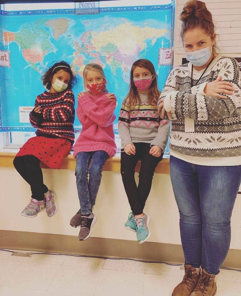 Enseignante et trois élèves posent en salle de classe avec leurs chandails de laine
