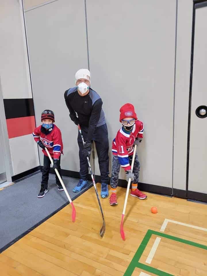Deux éleves et un enseignant posent pour la photo avec des bâtons d'hockey